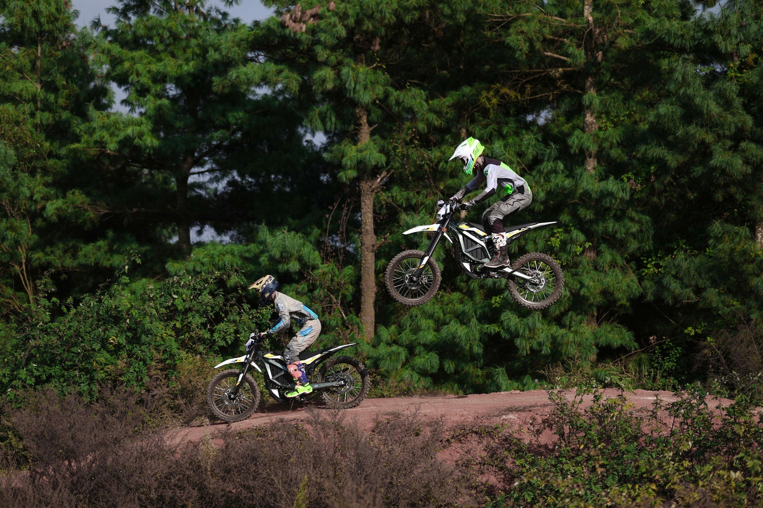 Deux pilotes en plein saut sur leurs motos Sur-Ron, illustrant l’excitation du comparatif Sur-ron Light Bee vs Ultra Bee dans un environnement tout-terrain.